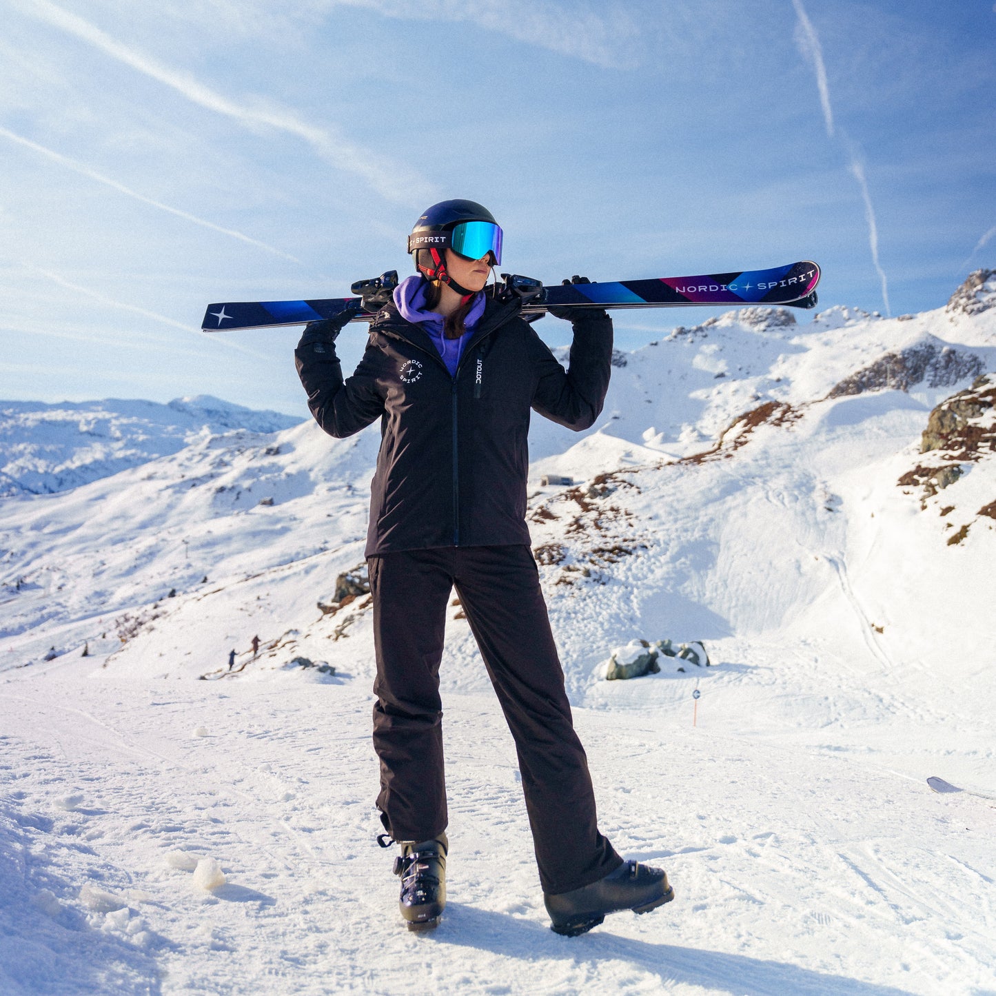 Eine Frau in Skiausrüstung steht auf einer Piste und hält ihre Nordic Spirit Skier auf den Schultern