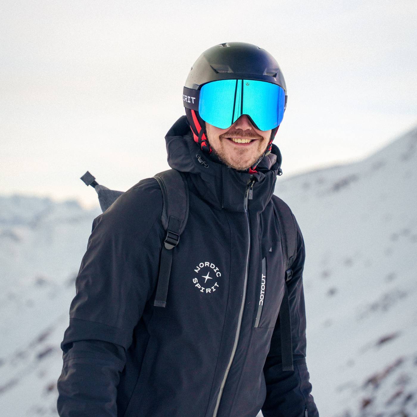 Ein lächelnder Mann mit Nordic Spirit Skibrille vor einem verschneiten Berghang