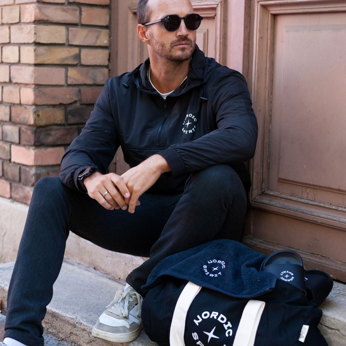 Person sitzt neben einer schwarzen Nordic Spirit Sporttasche und weiteren Nordic Spirit Accessoires.