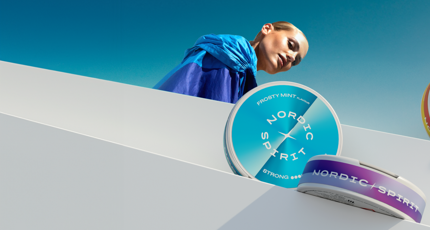 Person vor blauem Himmel mit zwei Nordic Spirit Dosen im Vordergrund – eine größere in Blau mit Frosty Mint Design, eine kleinere mit lila Farbverlauf.