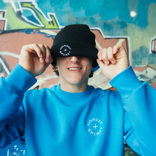 Junger Mann mit Nordic Spirit Beanie aufgesetzt vor Grafitti Wand