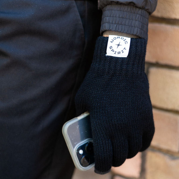 Schwarzer Strickhandschuh mit Nordic Spirit Logo hält ein Smartphone.