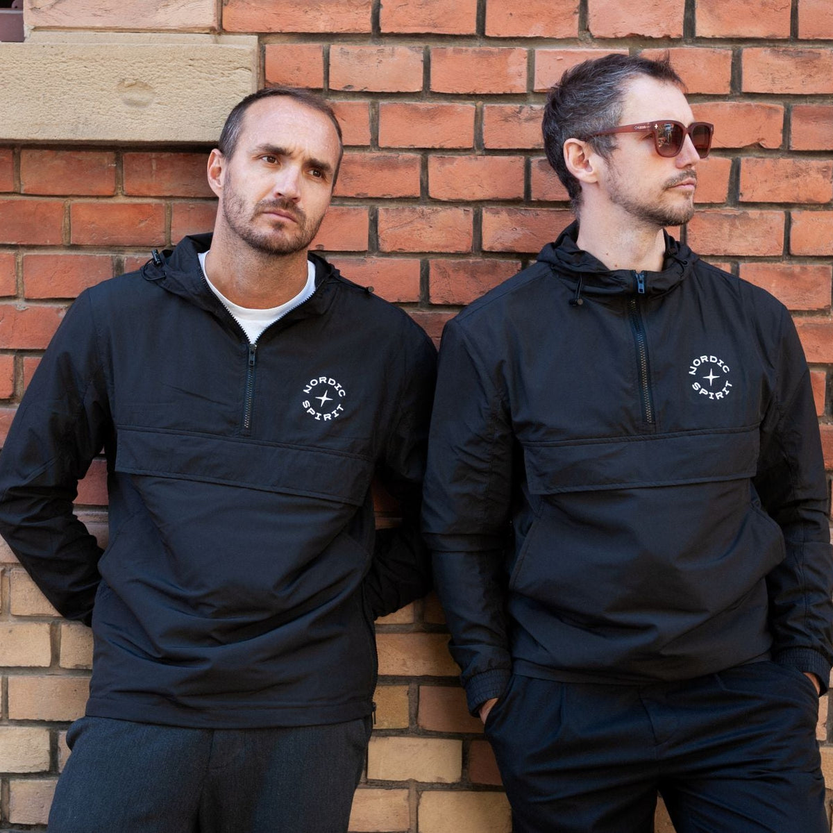 Zwei Personen mit Nordic Spirit Windbreakern vor Ziegelwand