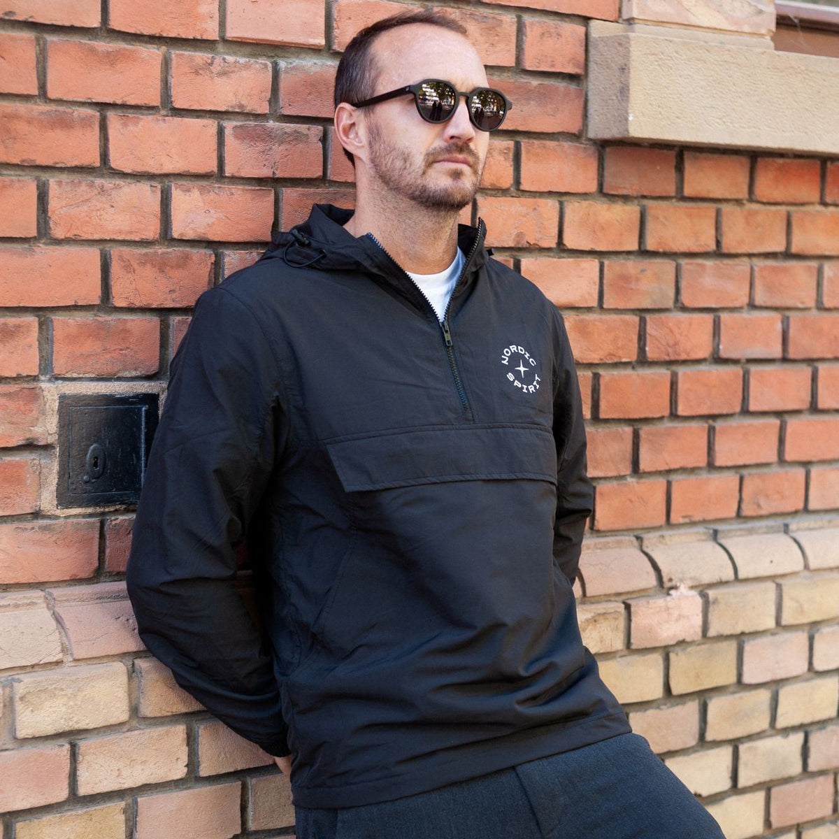 Person in Nordic Spirit Windbreaker mit Logo vor Ziegelwand.