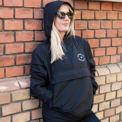 Person in Nordic Spirit Windbreaker mit Kapuze und Logo vor Ziegelwand.